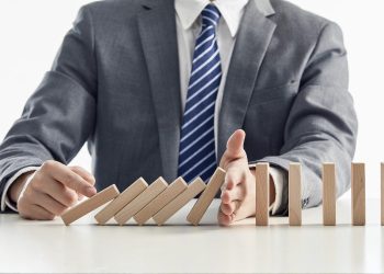businessman suit protecting wooden blocks from falling domino effect